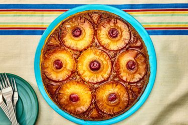 Overhead angle of pineapple upside down cake on a blue plate. The table cloth is a natural tone with blue, red, yellow and green stripes on the top. 